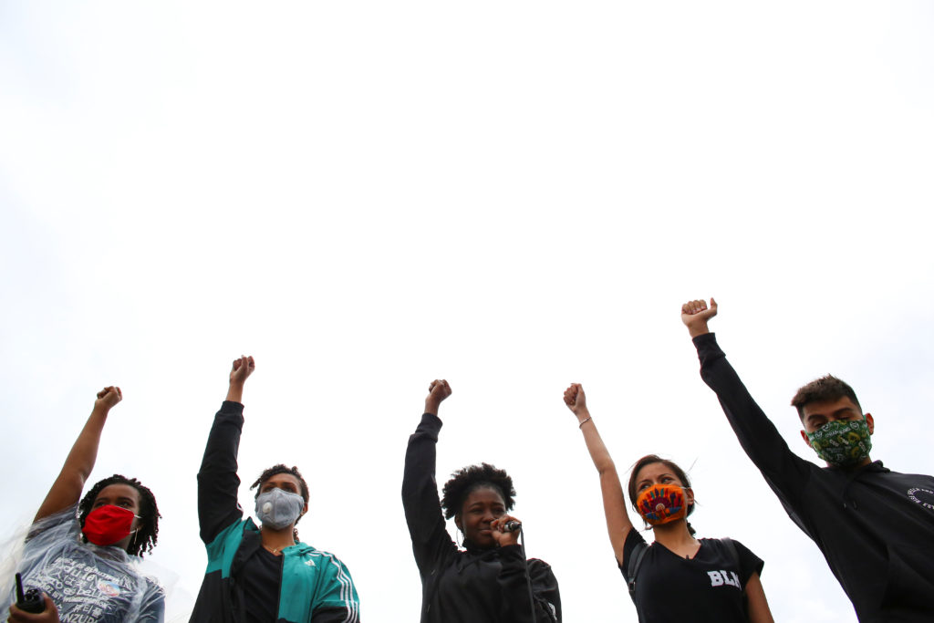 Five young Black Lives Matter protesters hold their right arms, fists clenched, in the air.