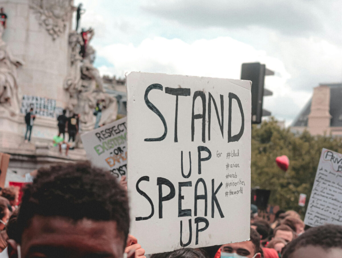 A protest sign that reads Stand Up Speak Up