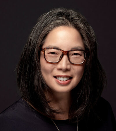 photo of person with black hair, glasses and black top against a dark background