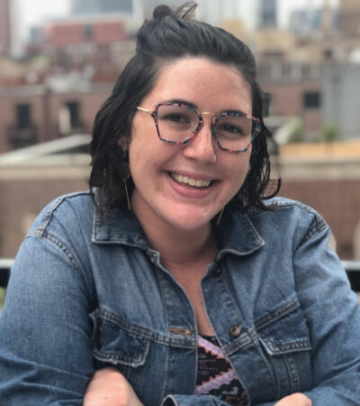 photo of person with dark brown hair, glasses and denim jacket smiling