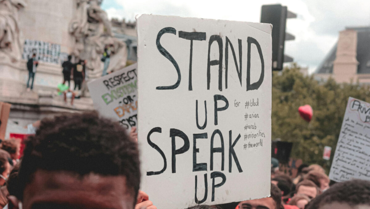 A protest sign that reads Stand Up Speak Up