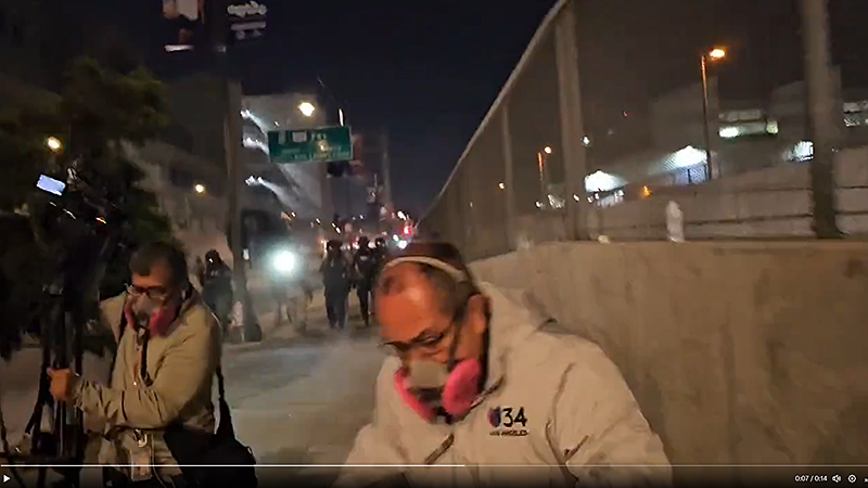A TV news camera crew runs from federal officers firing pepper balls at them.