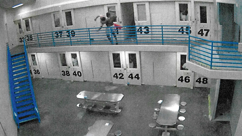 A surveillance camera still depicting a jail inmate throwing another jail inmate over a railing.
