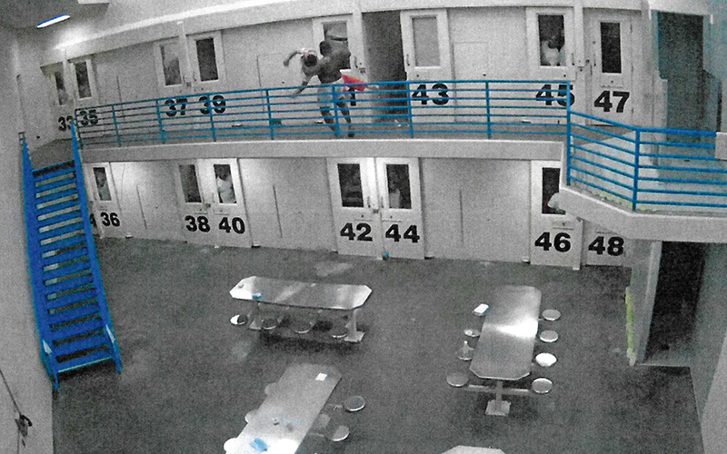 A surveillance camera still depicting a jail inmate throwing another jail inmate over a railing.
