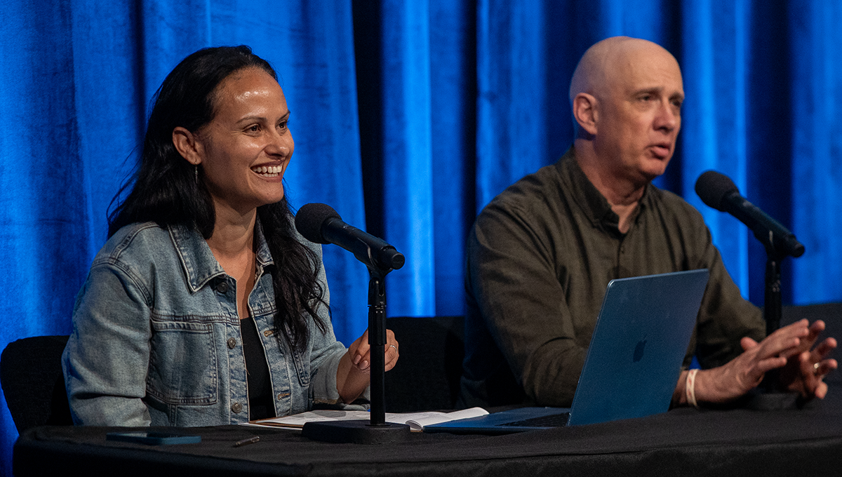A photo of a man and woman seated at a table with microphones.