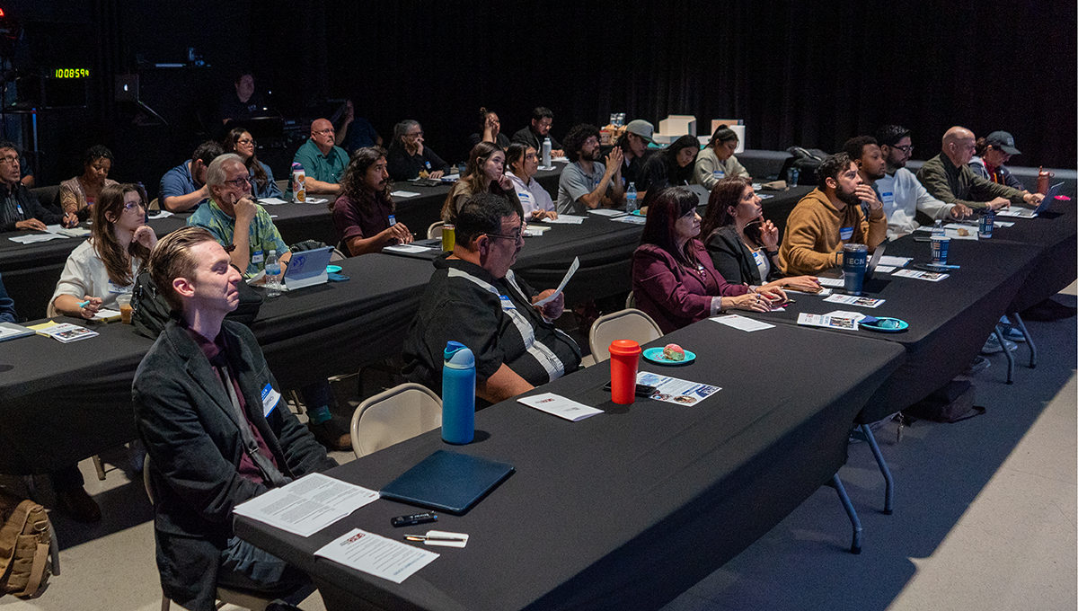 photo of workshop participants sitting in a black-draped room with black tablecloths.
